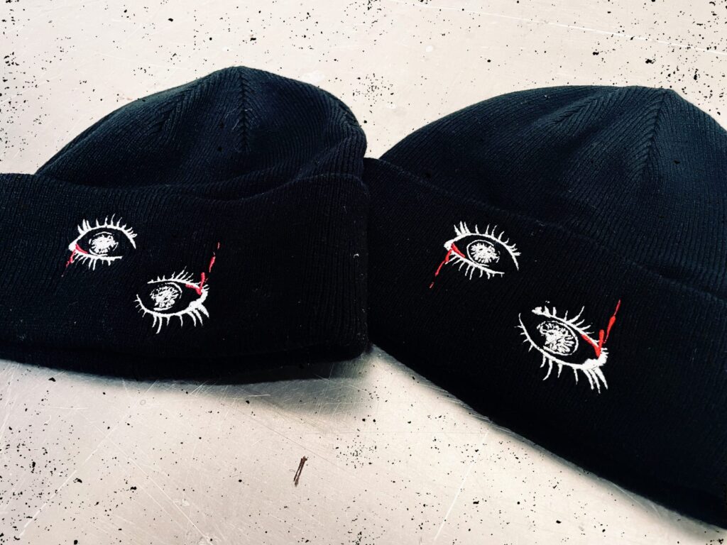 Two navy blue cuffed beanies featuring embroidered white eyes crying red tears of blood