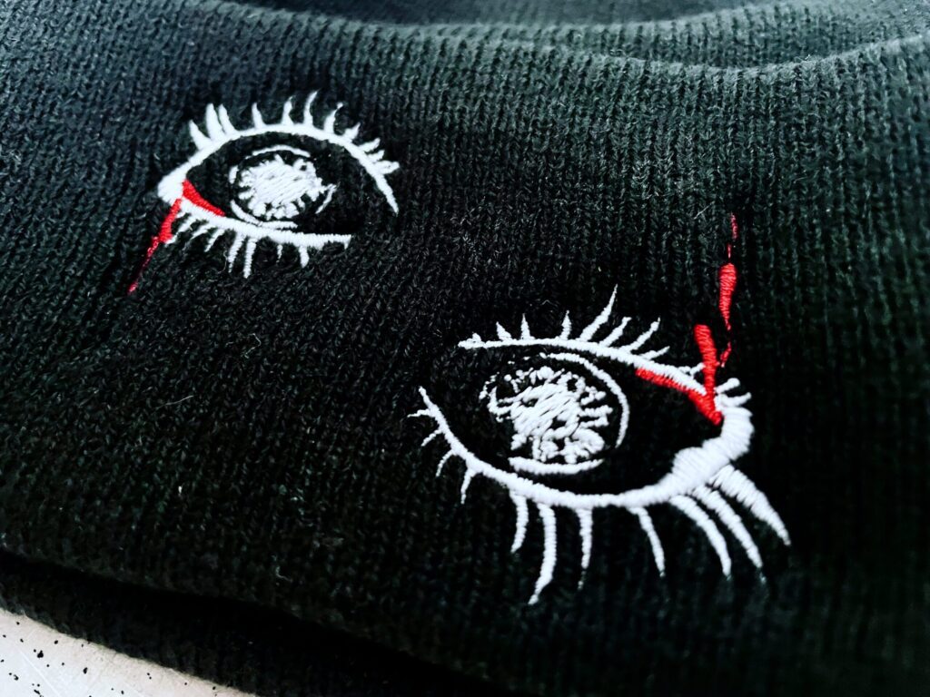 Navy blue cuffed beanie featuring embroidered white eyes crying red tears of blood